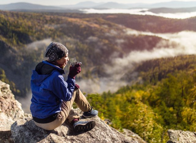 female hiker demonstrating the hiking habits that slow aging, sipping tea atop mountain