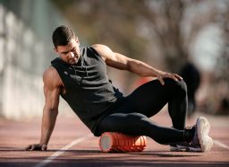 fit man doing foam rolling exercises for lower back pain on track