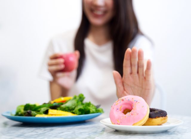 girl pushing donuts away, choosing salad instead, and holding a drink