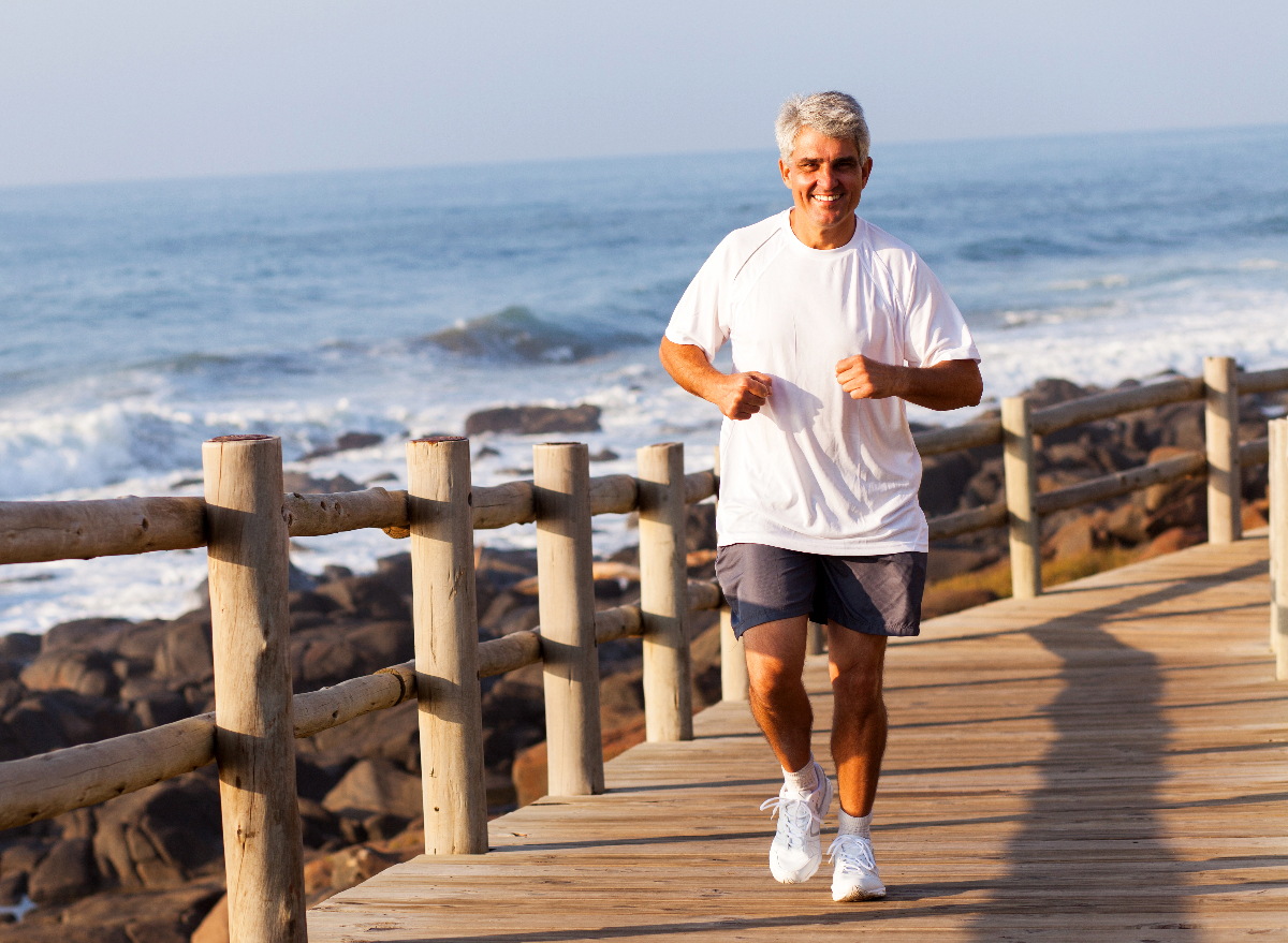happy, fit, mature man demonstrating the cardio habits that slow aging by running along beach