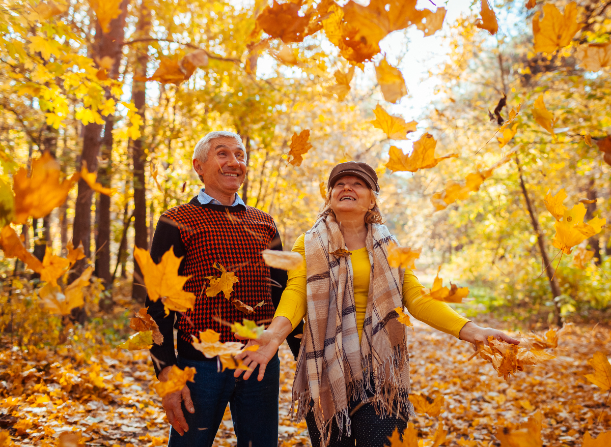happy senior couple tossing autumn leaves, demonstrating healthy habits to live to 100