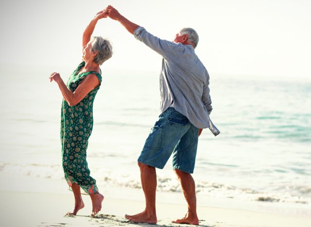 happy senior couple dances on the beach