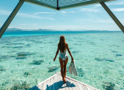 woman carrying snorkeling gear down dock on tropical trip, demonstrates how incredibly healthy people stay fit while traveling