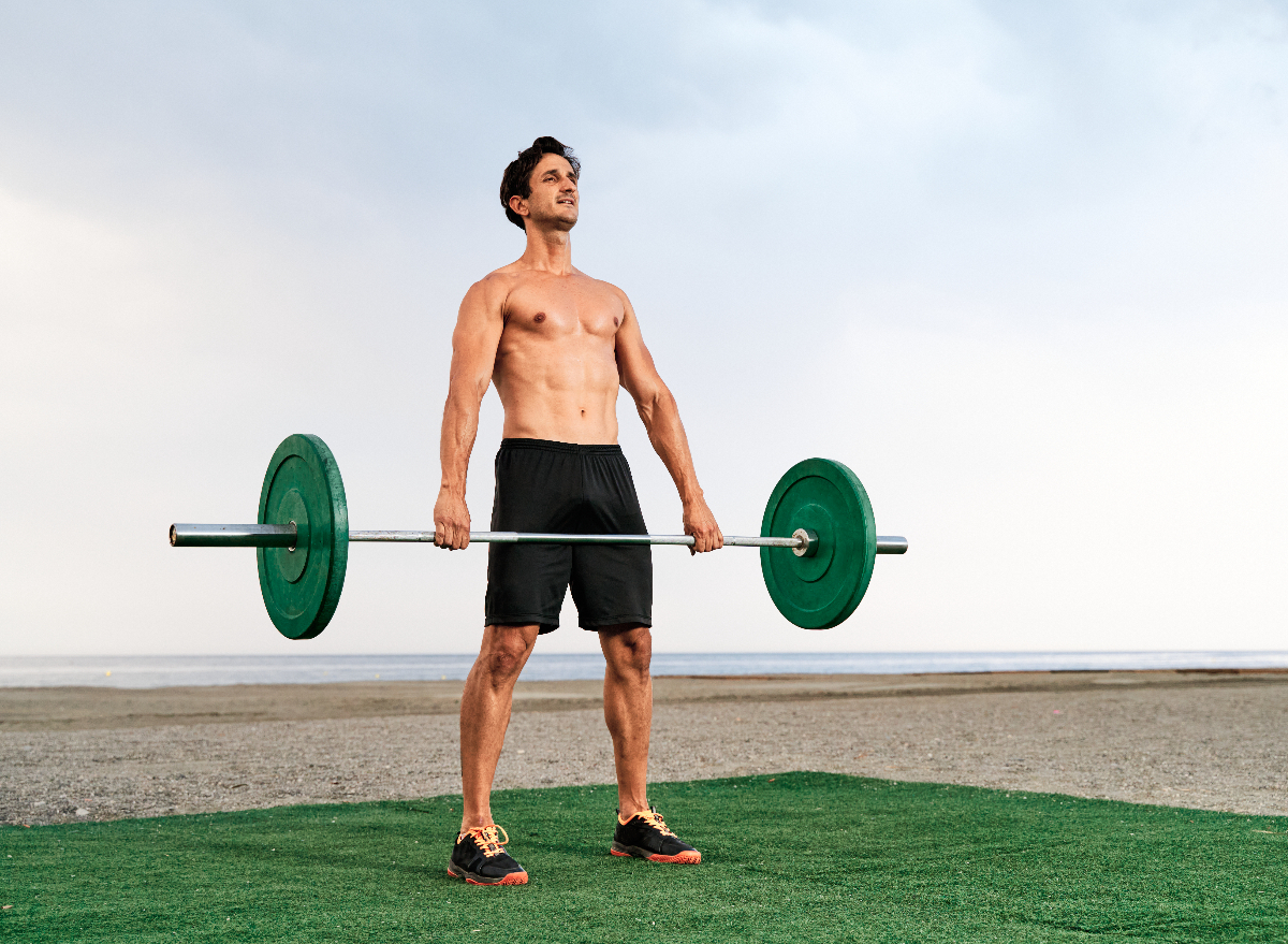man performing barbell exercise on turf by the beach to lose belly fat and slow aging