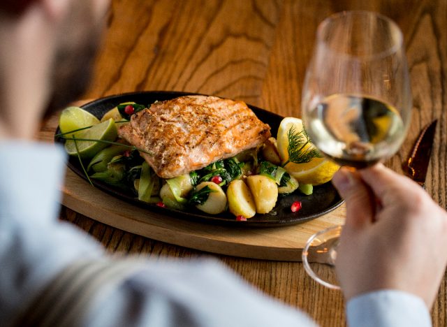 Man holding white wine and eating salmon, potatoes, and spinach