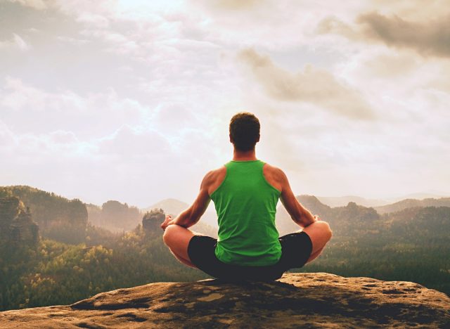 man peacefully meditates atop mountain, staying relaxed while traveling
