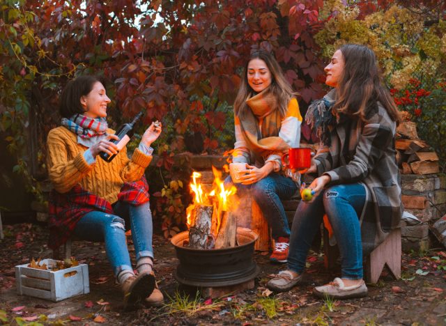 mature female friends drink by campfire on fall camping trip