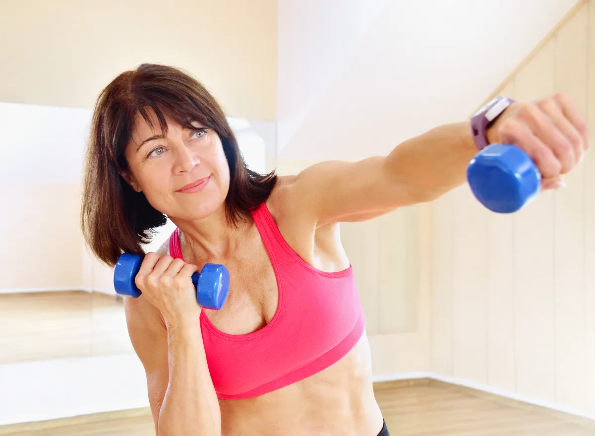 Young beautiful girl with big breasts and good figure in sports hall with  dumbbells in hands Stock Photo