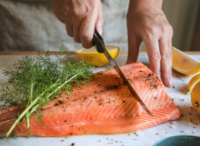 People slicing fresh salmon with dill and lemon