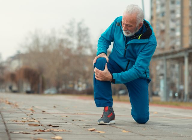 senior man dealing with knee pain while exercising outdoors