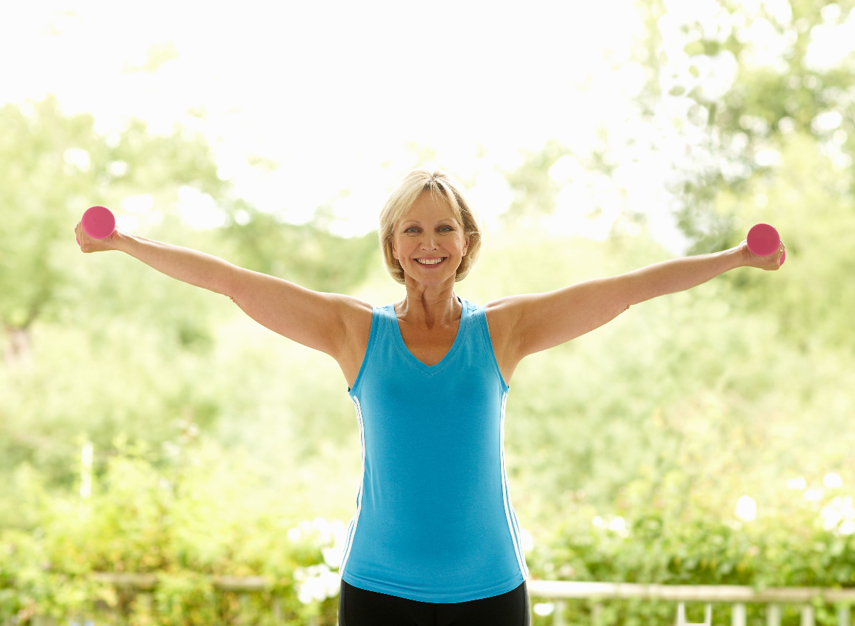 woman holding dumbbells doing bat wings workout outside on sunny day