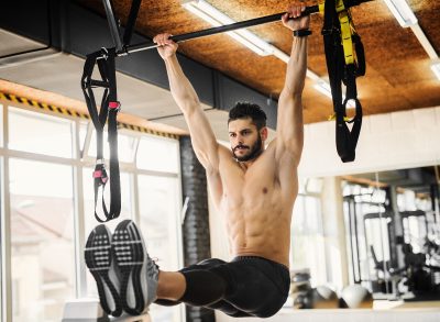 man hanging onto pull-up bar performing workout to flatten your stomach