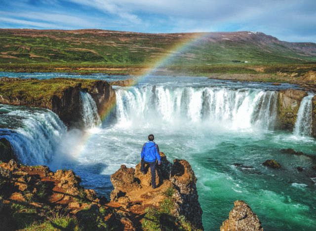 man standing by Godafoss waterfall in Iceland with rainbow