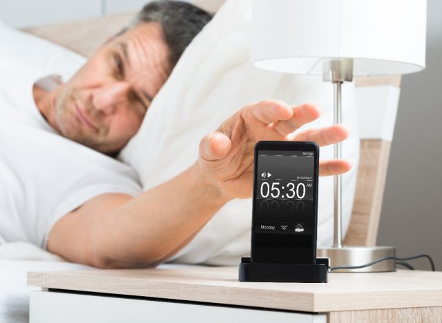 tired man turning off his morning alarm in bed