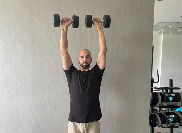 trainer demonstrating overhead press as part of workout for stronger muscles in your 50s