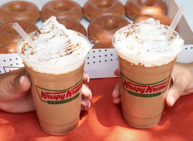 people holding krispy kreme's pumpkin spice lattes in front of doughnut box