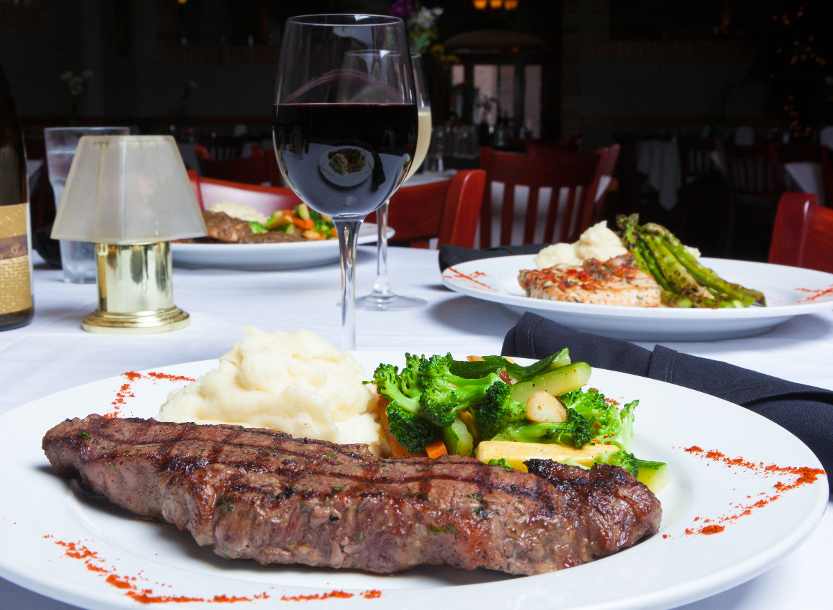 plate with steak, mashed, potatoes, and vegetables next to glass of red wine