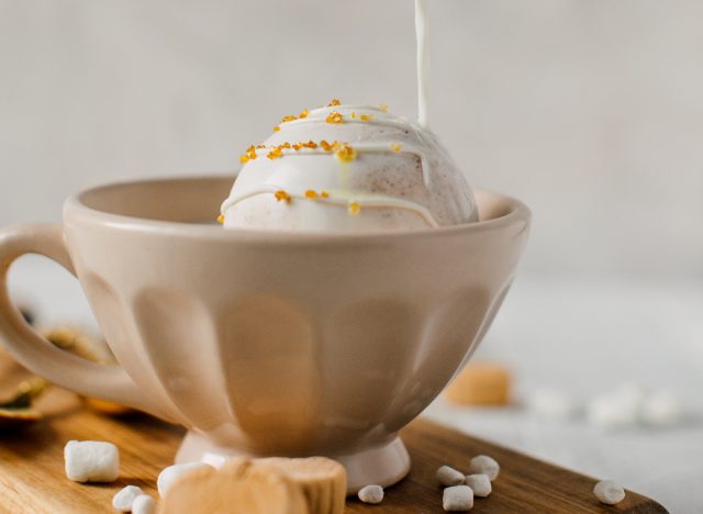 pouring milk over white chocolate hot cocoa bomb in cup