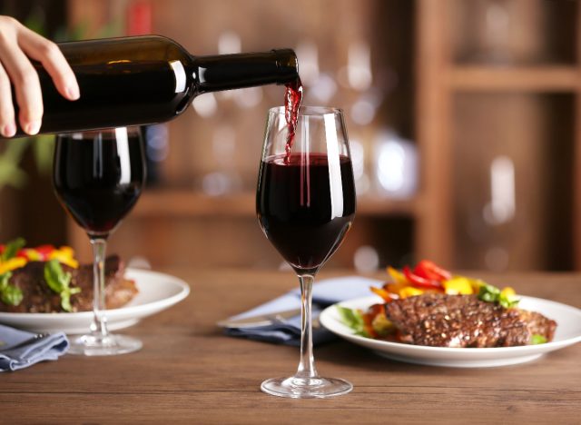 pouring red wine into glass next to steak