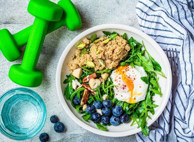 quinoa salad with poached egg, nuts, and blueberries next to dumbbells and water