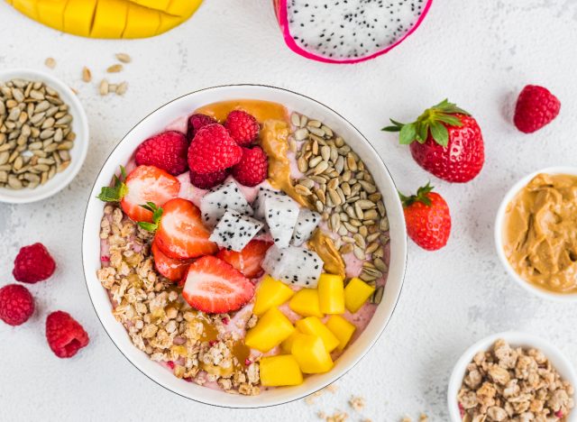 smoothie bowl with strawberries, raspberries, mango, dragon fruit, peanut butter, sunflower seeds, and granola