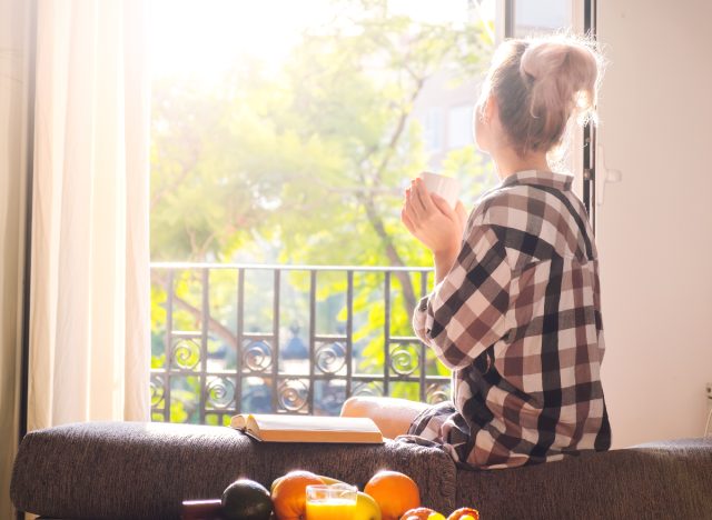 Woman sipping morning coffee in bright room with sunrise stream in