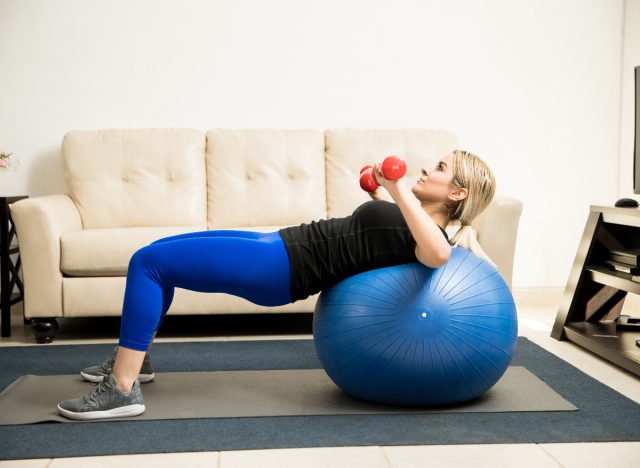 woman performing dumbbell chest press on exercise ball during workout for a smaller waist