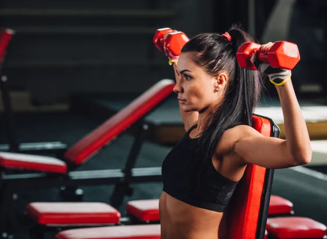 woman performing dumbbell shoulder press workout for a smaller waist