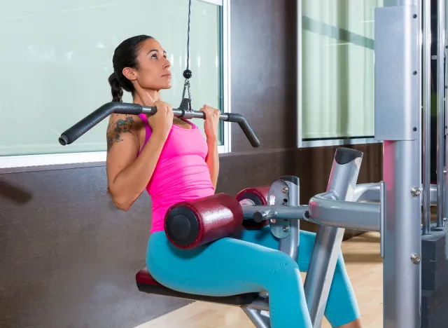 woman doing lat pulldowns at gym to lose back fat