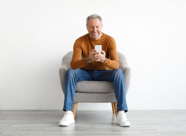 mature man sitting in chair, happy, texting