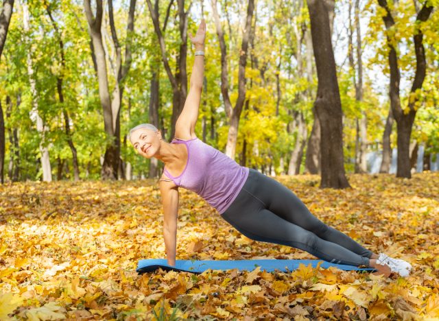 Mature woman performing side plank in fall leaves to slow muscle aging