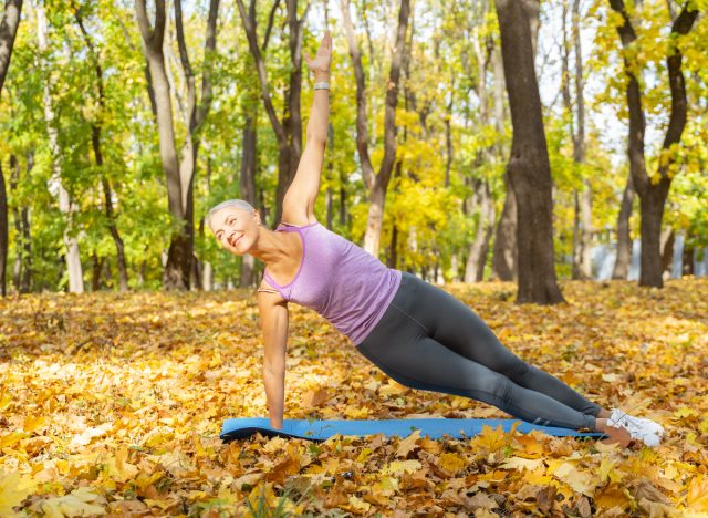 mature woman performing side plank in autumn leaves to slow muscle aging