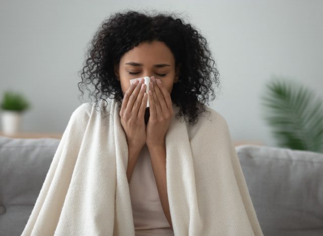 woman blowing her nose, sick at home cold weather