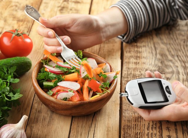 woman eating salad while holding glucometer