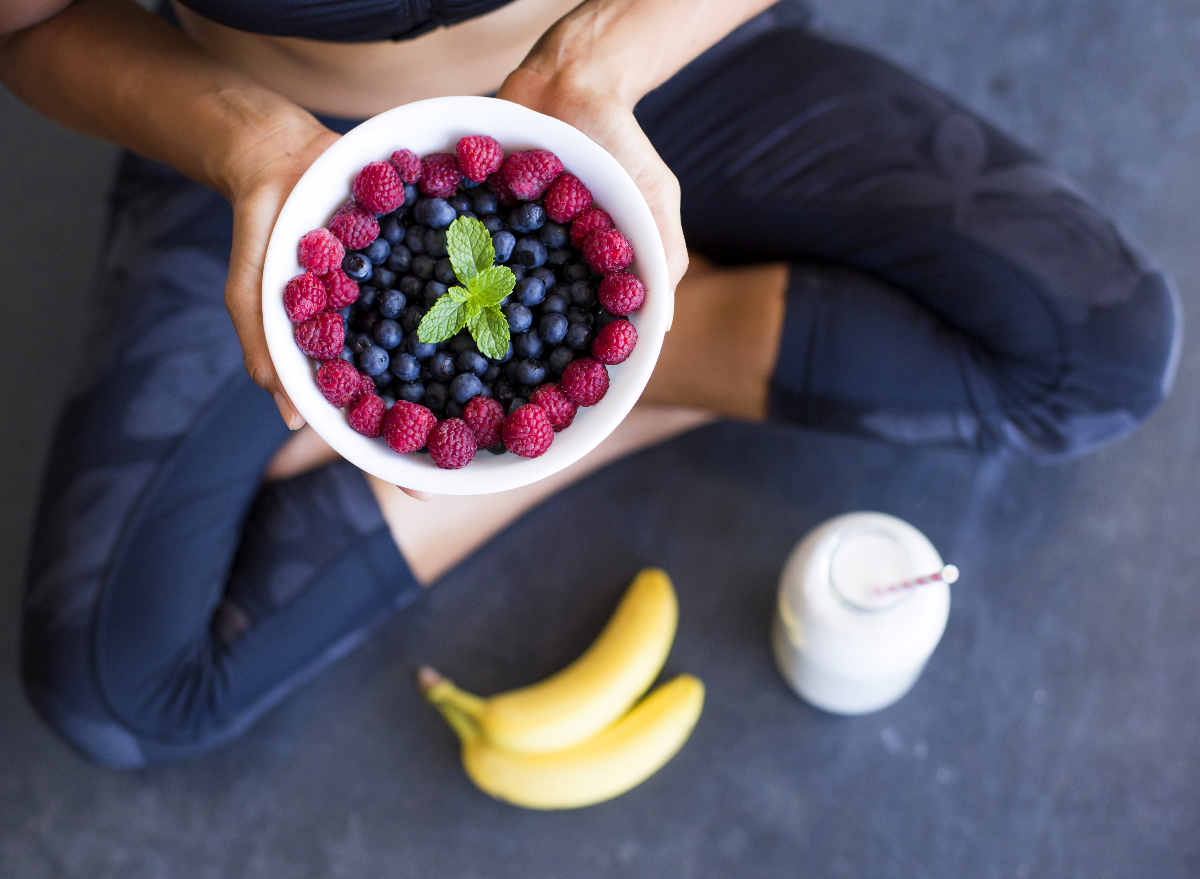 fitness woman holding bowl of berries, fruits to get rid of abdominal fat