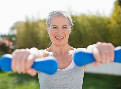 woman exercising with free weights outdoors, demonstrating exercises to regain muscle mass after 60