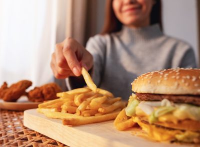 woman holding french fry next to hamburger and fried chicken