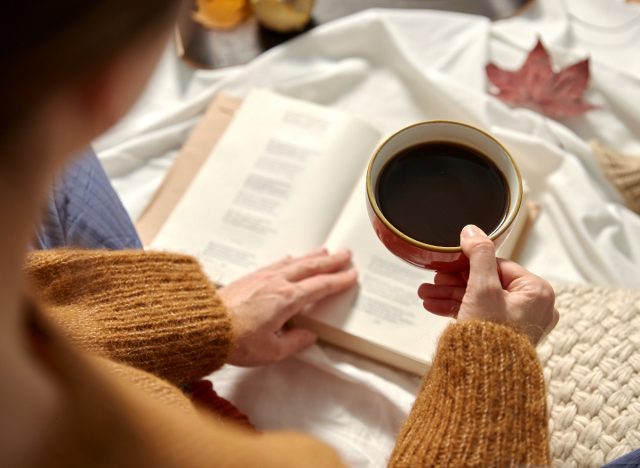 woman reading on picnic blanket while enjoying coffee, close-up, in autumn