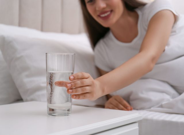 a woman taking a glass of water from the bedside table