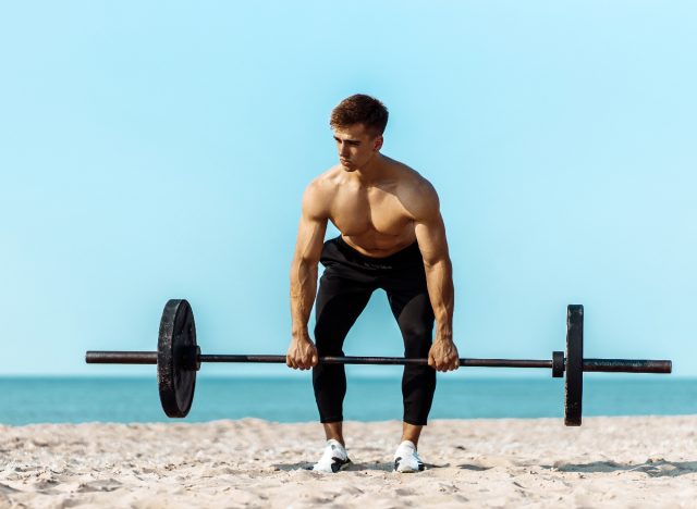 fitness man lifting a barbell on the beach