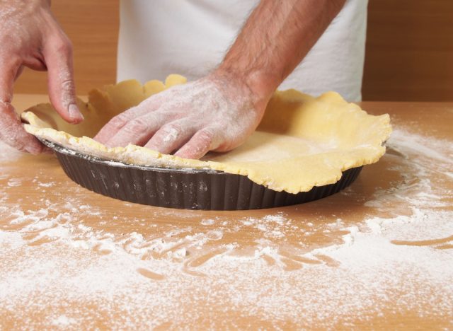 man pressing puff pastry onto tin