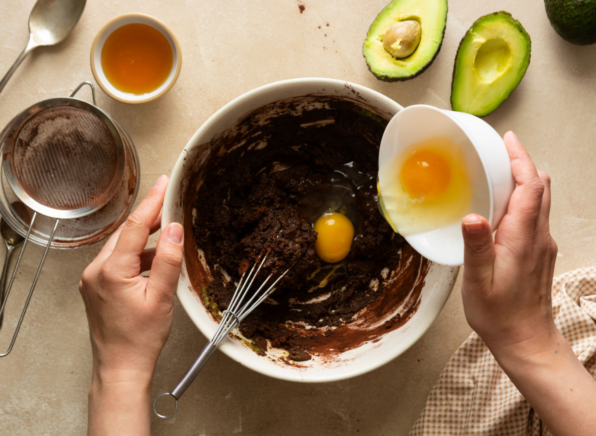 person pouring egg into avocado brownie batter