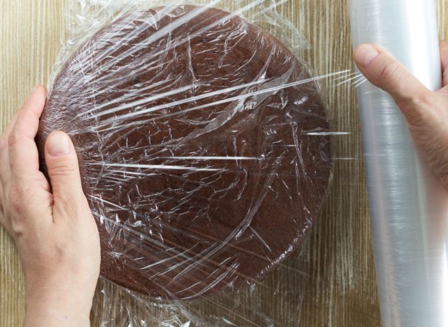 person wrapping chocolate sponge cake with plastic wrap