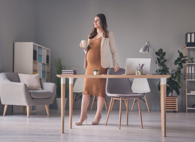 Pregnant woman standing at desk with cup of coffee