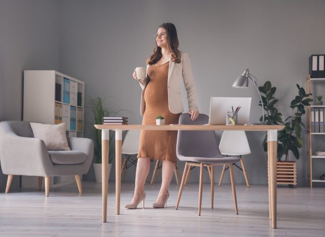 pregnant woman standing at desk with coffee mug