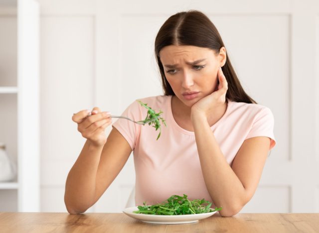 sad woman eating lettuce, food restriction concept