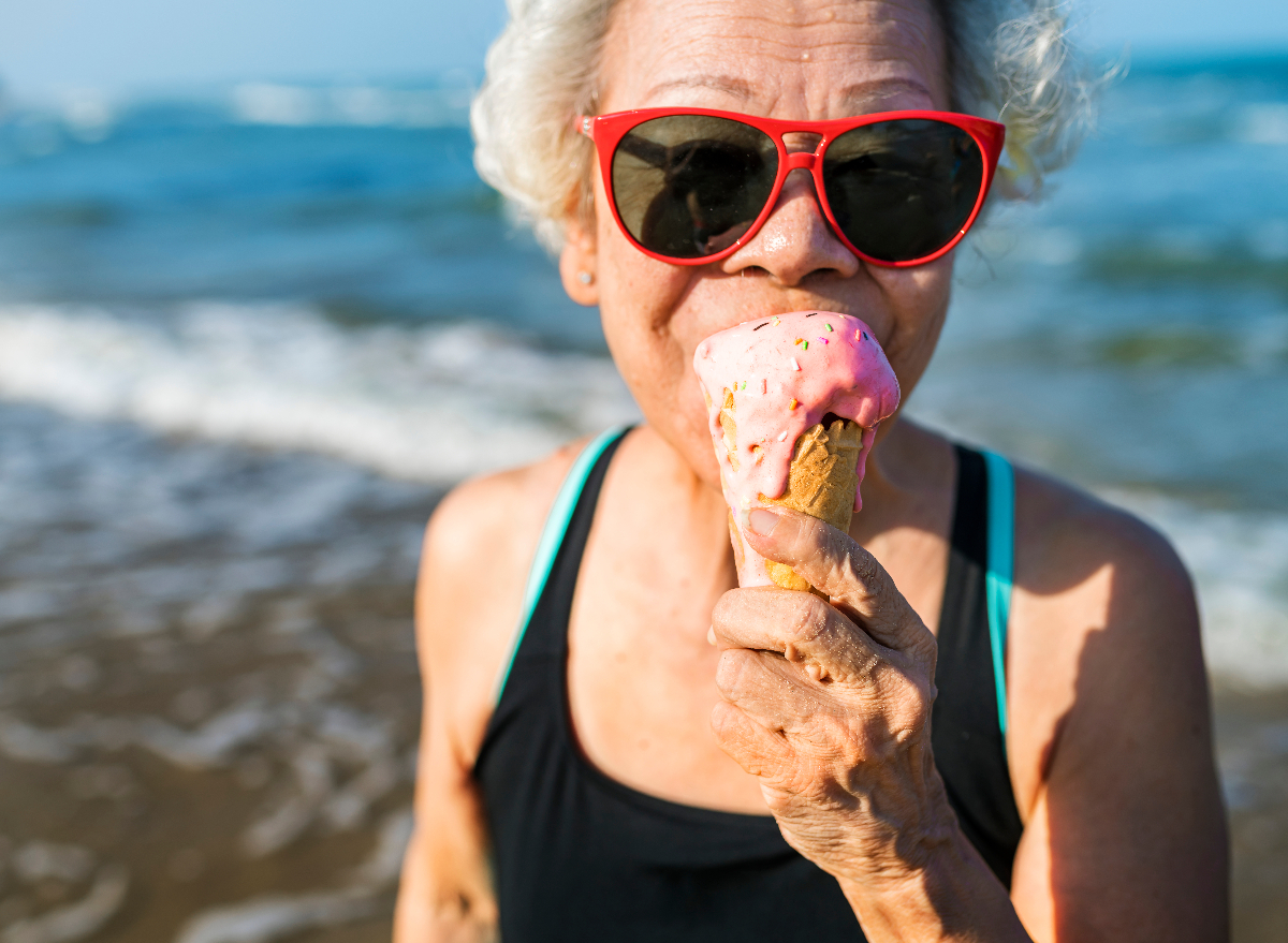 senior woman eating ice cream on beach demonstrating secrets to live to 100 concept