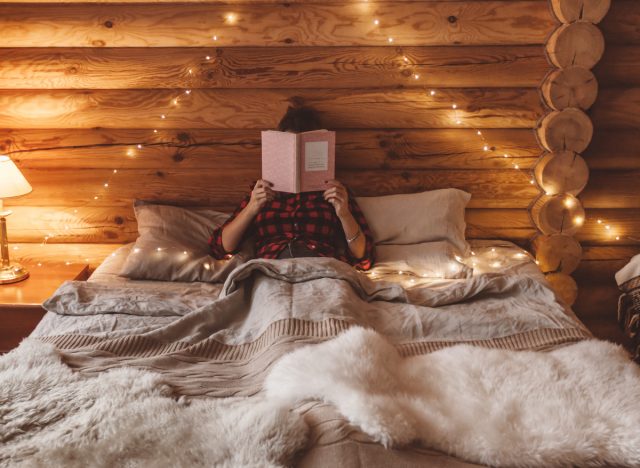 cozy woman in bed reading a book, winter cabin