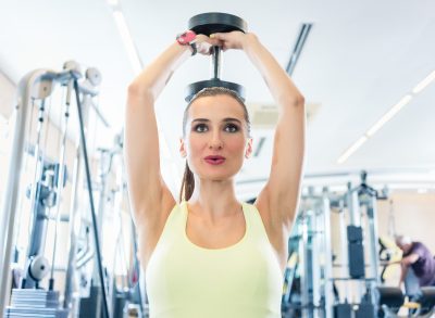 woman performing dumbbell exercises at the gym to lose arm fat