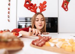festive woman enjoys holiday foods in kitchen, avoid weight gain